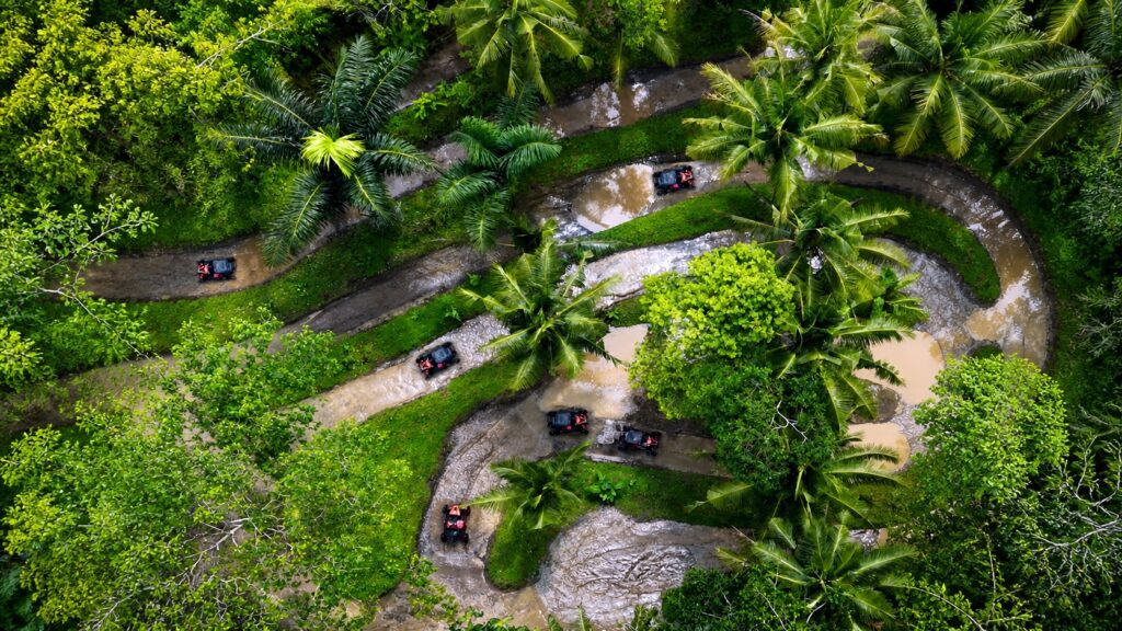 Drone view of UTV jungle buggies racing through muddy tropical off-road tracks at Pertiwi Adventure Bali